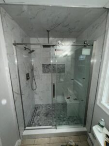 Glass-enclosed shower with porcelain wall tile and mosaic tile flooring, featuring built-in bench and rainfall showerhead.