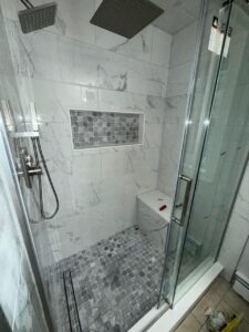 Close-up of porcelain tile shower with mosaic tile niche, rainfall head, and corner bench for modern, functional bathroom design.