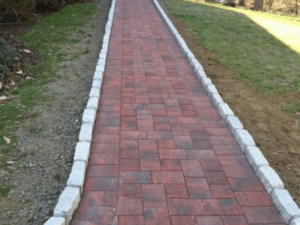 Red paver sidewalk installation featuring stone edging for enhanced durability, elegant visual appeal, and safe, accessible foot traffic flow.