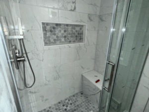 Close-up of porcelain tile shower with mosaic tile niche, rainfall head, and corner bench for modern, functional bathroom design.