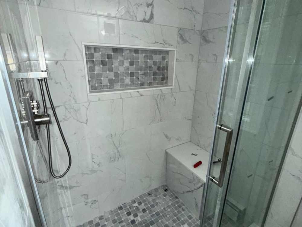 Close-up of porcelain tile shower with mosaic tile niche, rainfall head, and corner bench for modern, functional bathroom design.