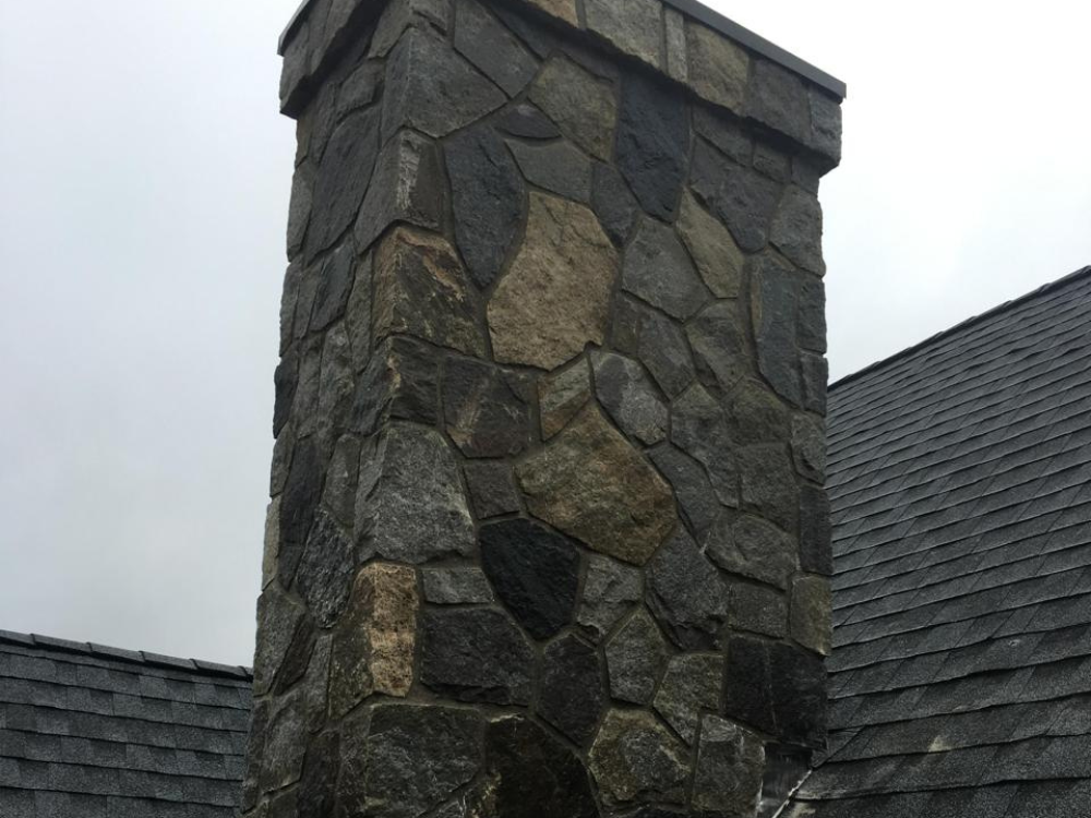 Stone chimney showcasing expert masonry solutions on a residential rooftop.