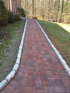 Long red paver walkway lined with granite stones through residential front yard
