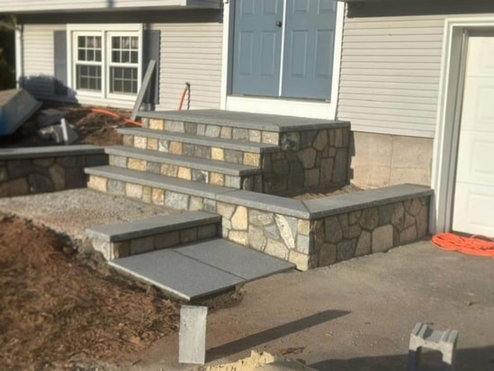Installation of stone veneer walls with granite steps during front entry renovation project