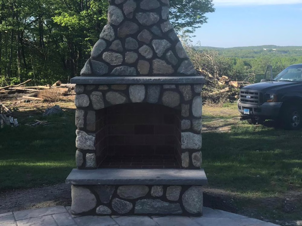 Custom stone outdoor fireplace with chimney in backyard