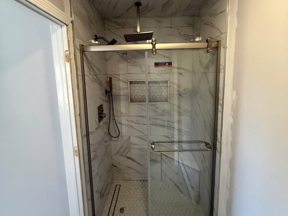 Luxury shower with marble wall tiles, frameless glass doors, and rain showerhead