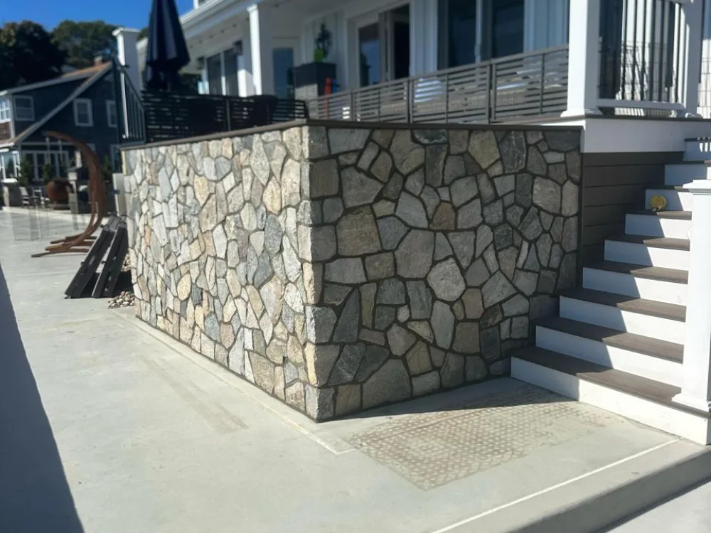 Stone retaining wall construction with natural stone finish, integrated stairs, and modern concrete exterior.