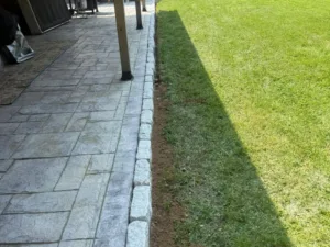 Stone patio edge installation creating a clean boundary between the paved patio and the lawn.