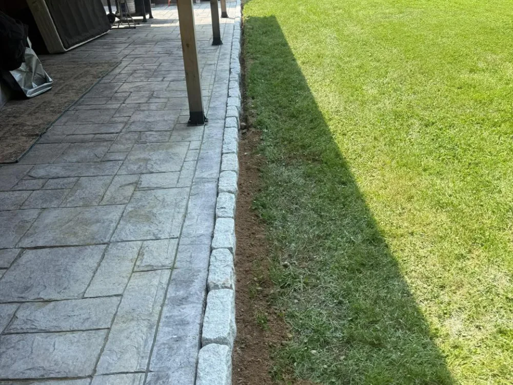 Stone patio edge installation creating a clean boundary between the paved patio and the lawn.